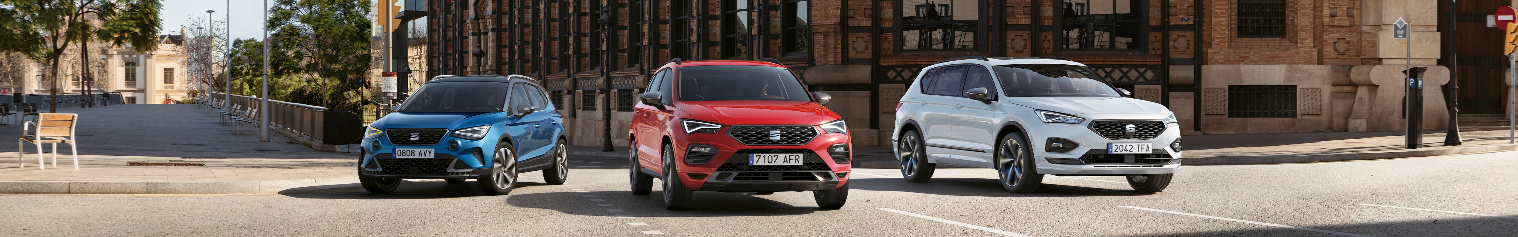 SUV-y SEAT: Arona w kolorze Sapphire Blue, Ateca w kolorze Desire Red i Tarraco w kolorze Urban Silver, zaparkowane na ulicy.