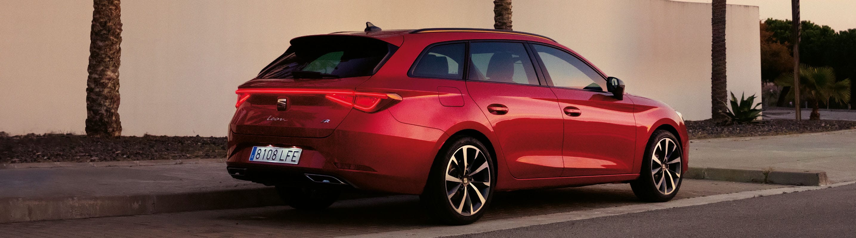 Zaparkowany Seat Leon w kolorze Desire Red z zapalonymi tylnymi światłami LED. 