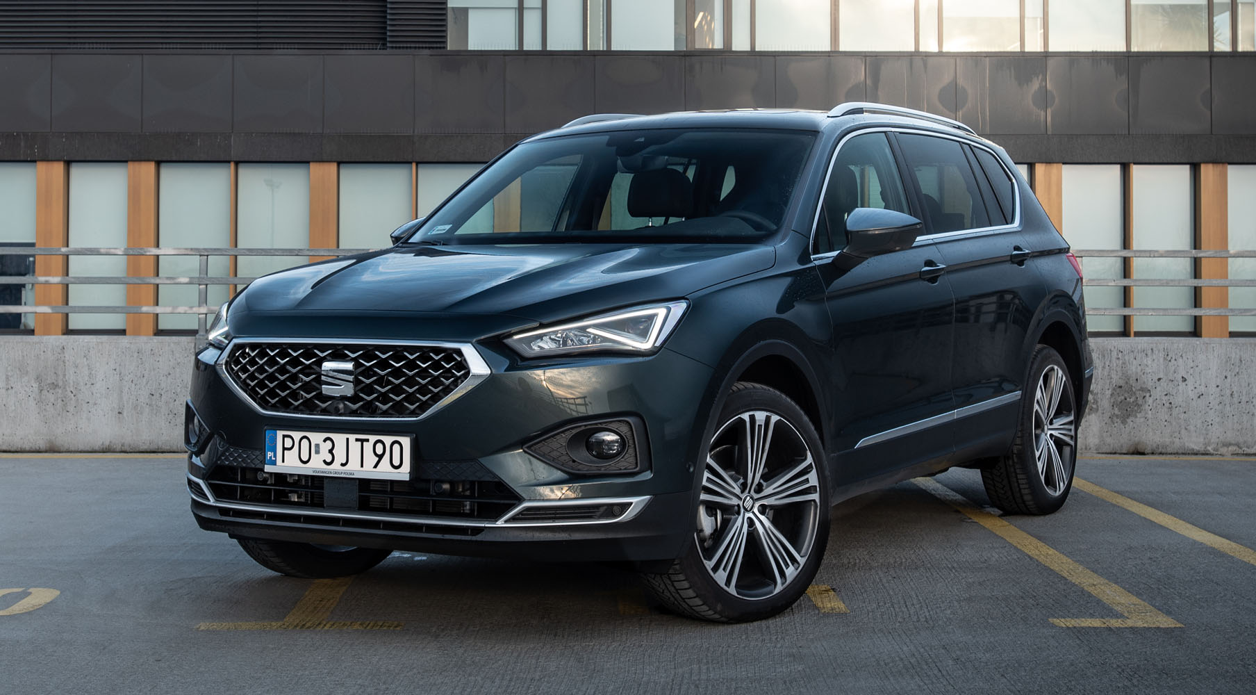 Zaparkowany Seat Tarraco w kolorze Dark Camouflage z zapalonymi przednimi światłami LED.