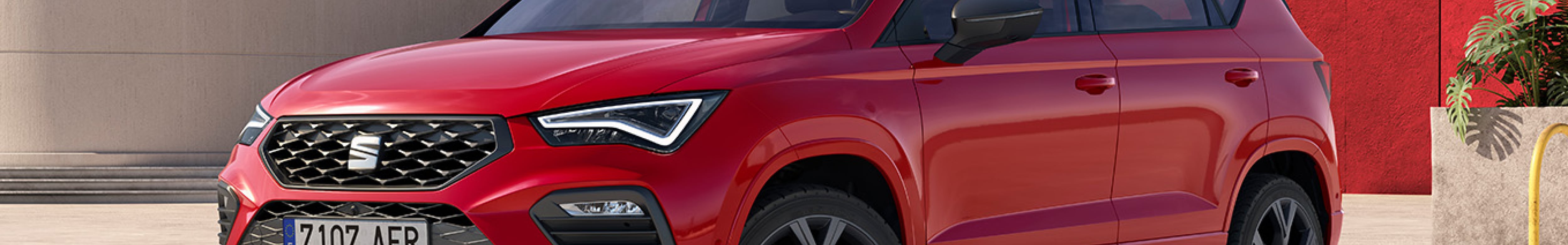 Zaparkowany SUV SEAT Ateaca  w kolorze Dark Camouflage z zapalonymi przednimi światłami LED, z miastem w tle.