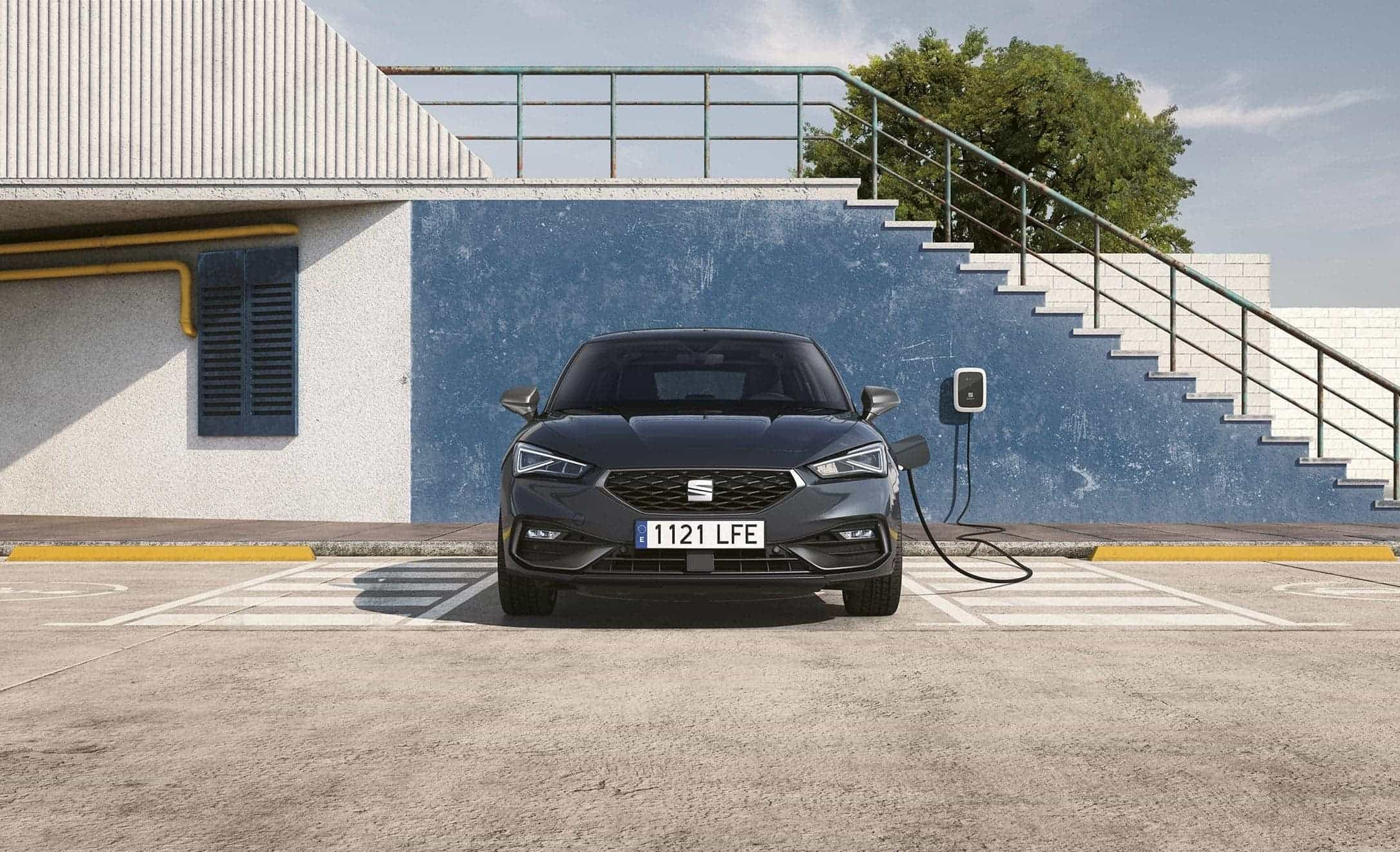 SEAT Leon e-HYBRID w kolorze Midnight Black podłączony do ładowarki, widziany z przodu. 