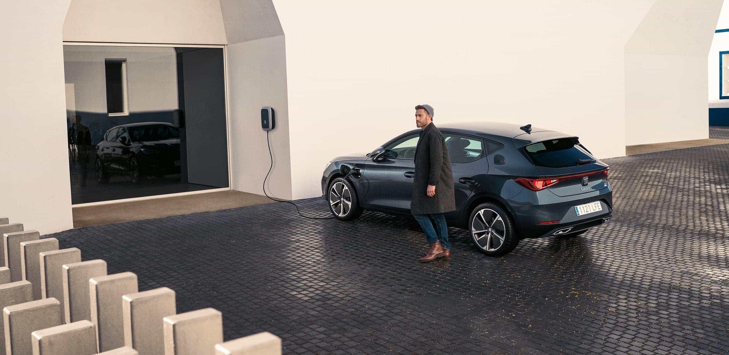 Czarny SEAT Leon e-HYBRID podłączony do ładowarki, widziany z boku. 