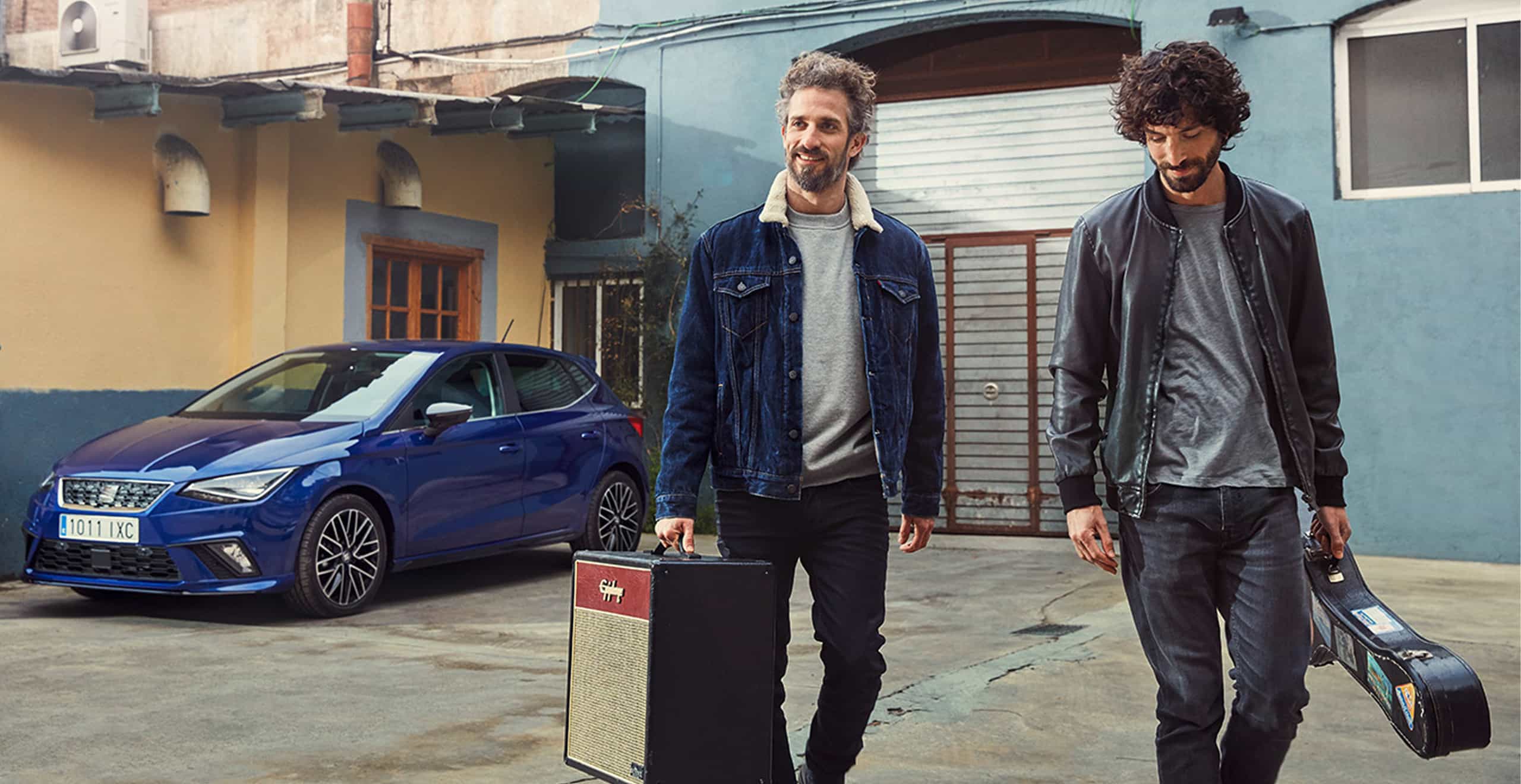 Dwóch mężczyzn niesie sprzęt muzyczny przy nowym modelu niebieskiego SEATa Ibiza z Beats Audio