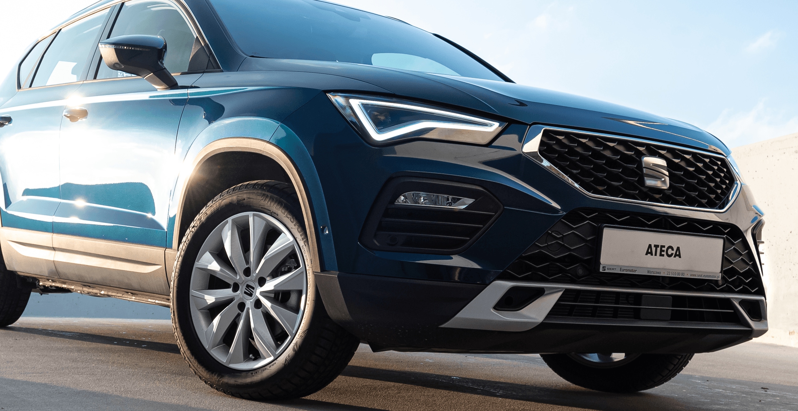 Zaparkowany SEAT Arona w kolorze Magnetic Tech, metalizowany. Widok z przodu na prawy profil. Zbliżenie na reflektor LED.