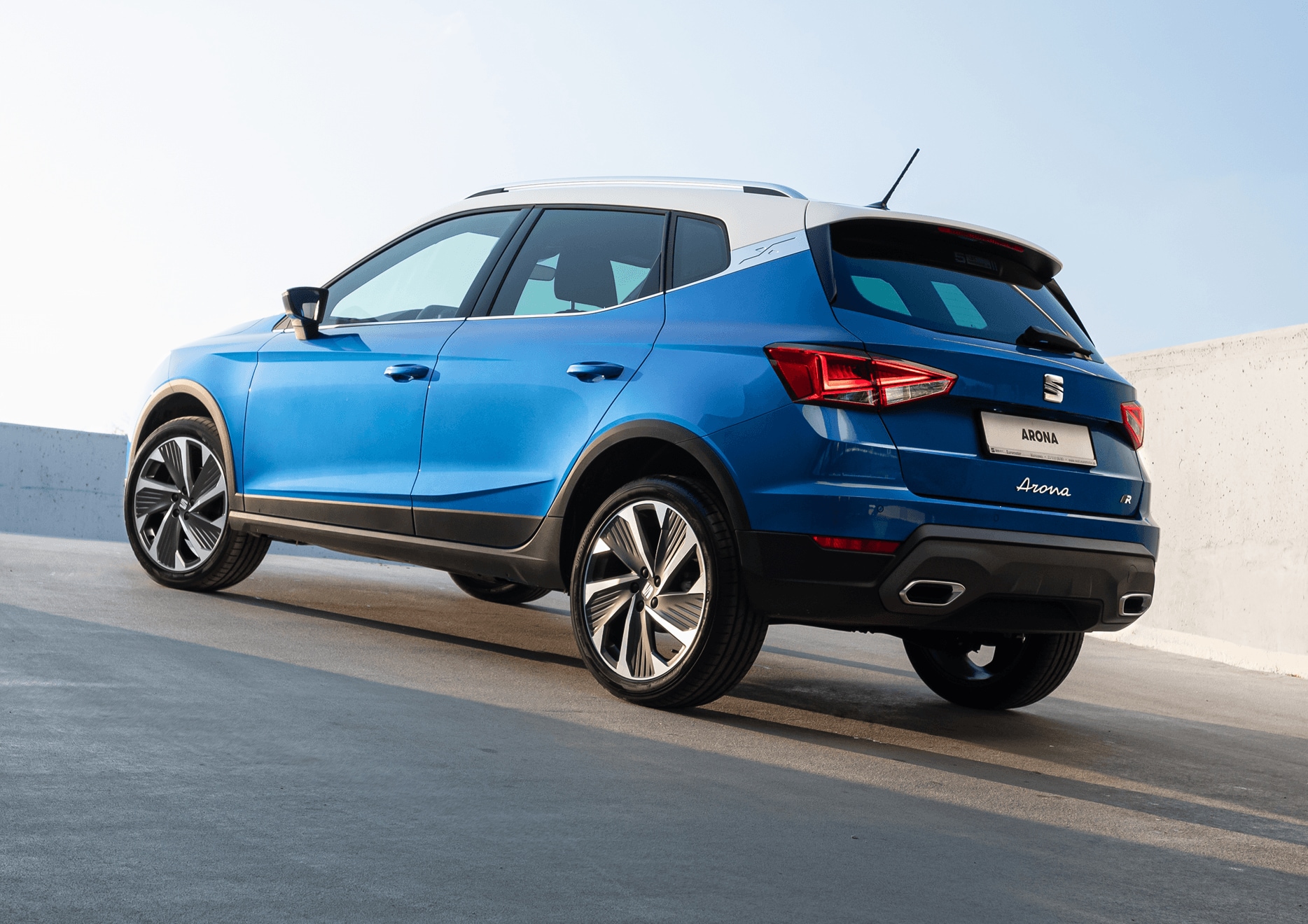 Zaparkowany SEAT Arona w kolorze Lava Blue, metalizowany, widok od tyłu, lewy profil. W świetle dziennym. Zaparkowany SEAT Arona w kolorze Lava Blue, metalizowany, widok od tyłu, lewy profil. W świetle dziennym.