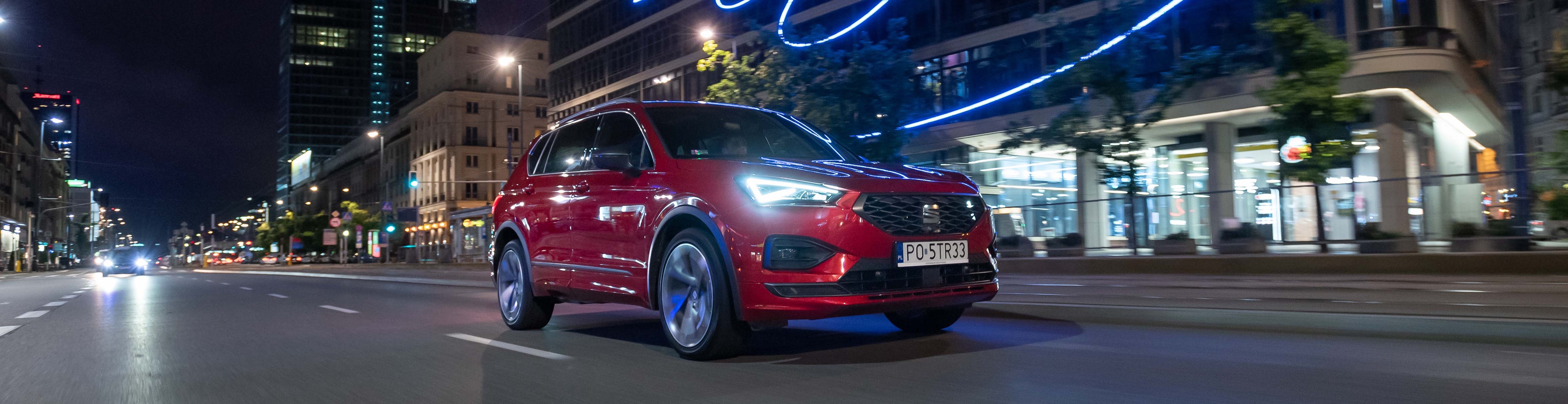 Czerwony SEAT Leon ze światłami full LED na parkingu, widok z lewego boku