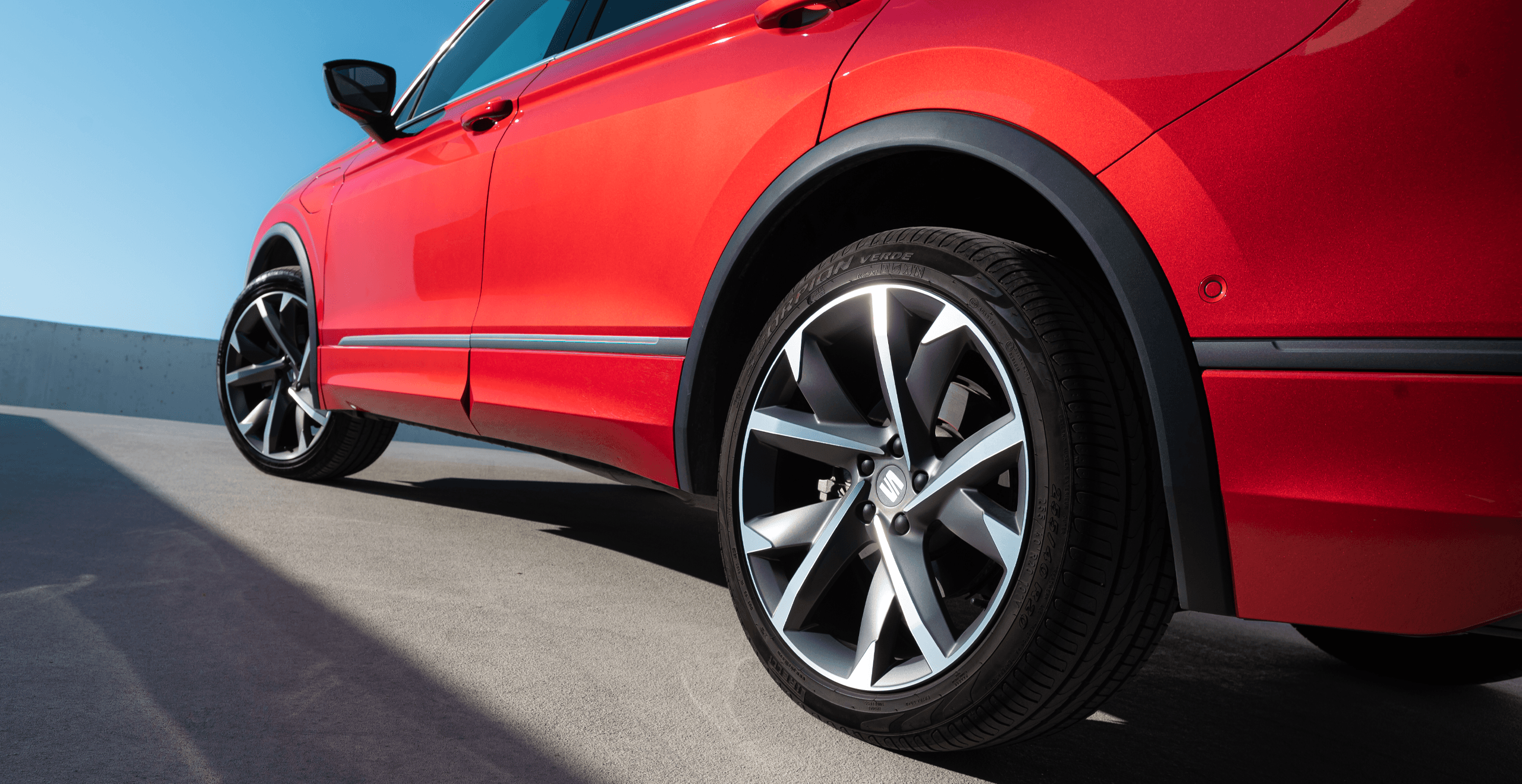 Zaparkowany rodzinny SEAT Tarraco w kolorze Desire Red, widok z tyłu na lewą stronę. Na pierwszym planie tylne koło.