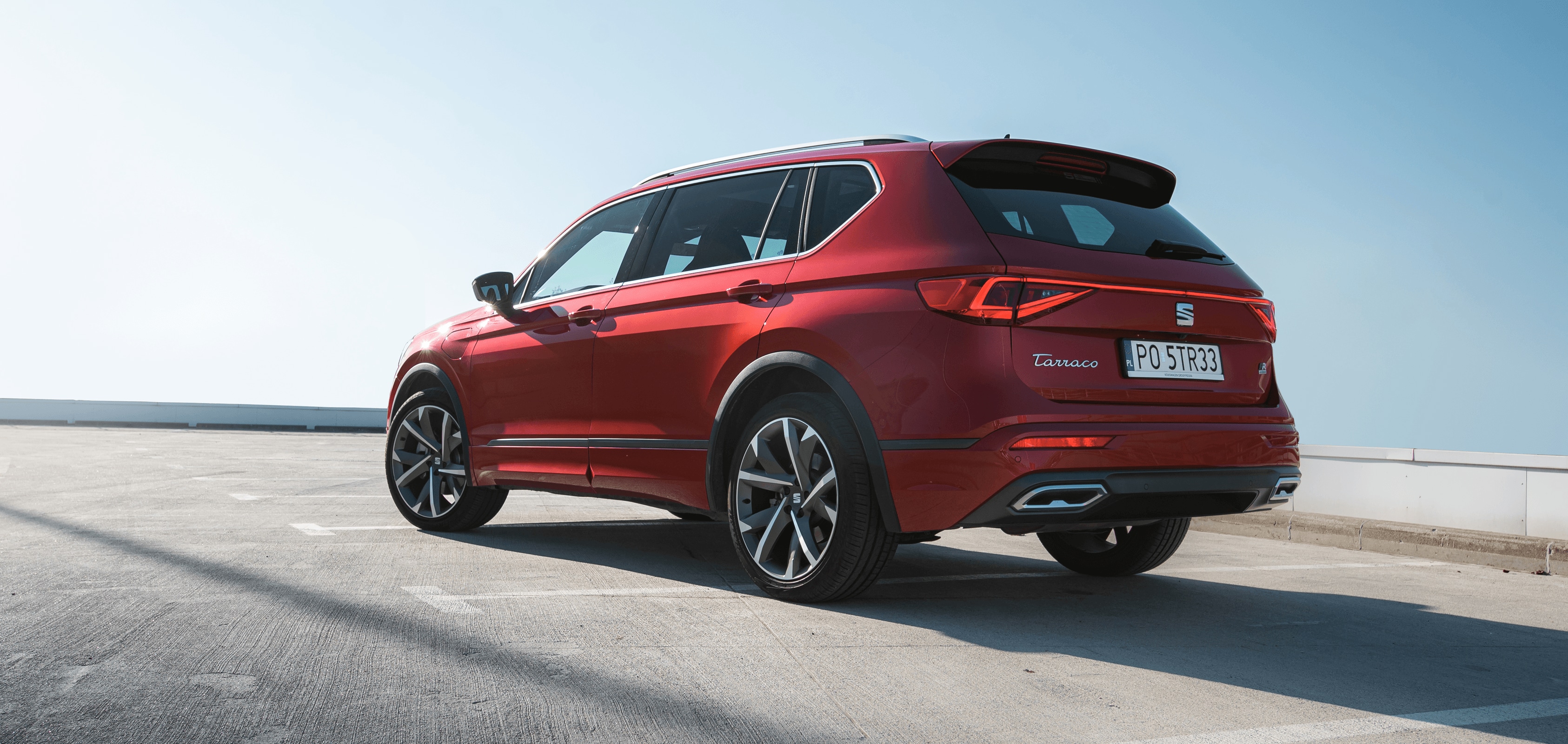 Zaparkowany SEAT Tarraco w kolorze Desire Red, widok z tyłu na lewą stronę. W świetle dziennym. 