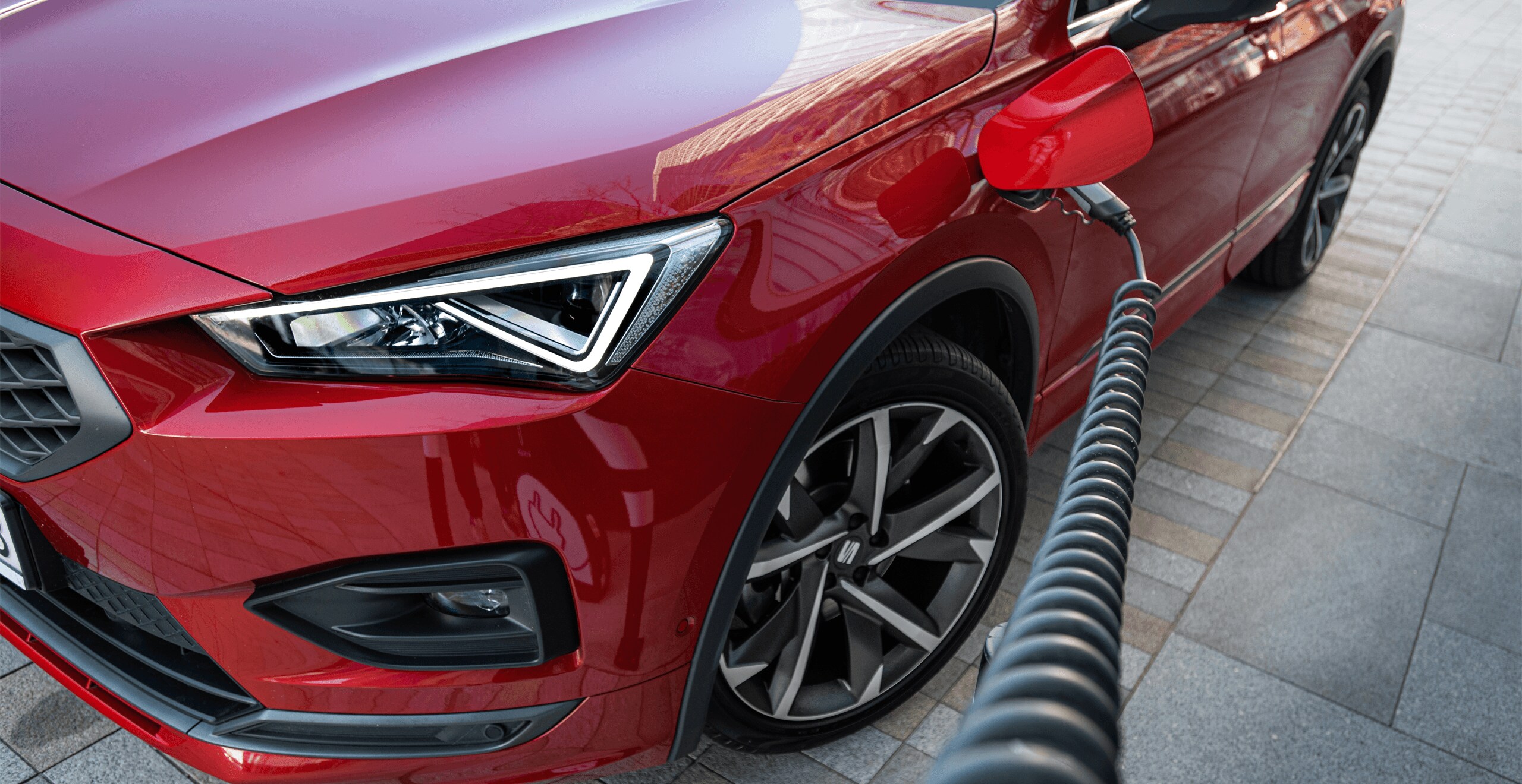 SEAT Tarraco e-Hybrid w kolorze Desire Red, metalizowany. Podłączony do stacji ładowania. Światło dzienne, miasto.