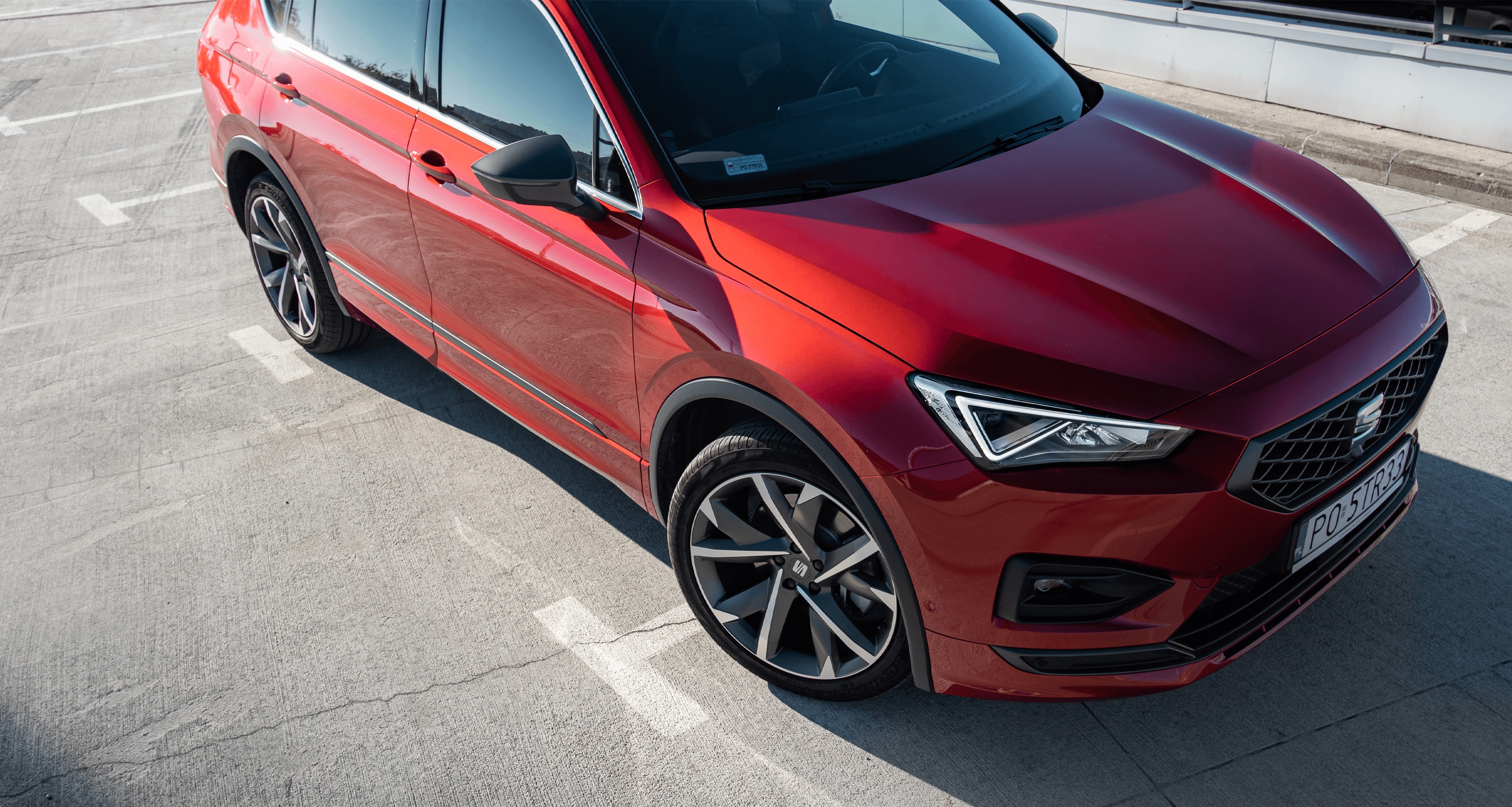 Zaparkowany SEAT Tarraco w kolorze Desire Red, metalizowany. Widok z góry na prawą stronę auta. Światło dzienne. 