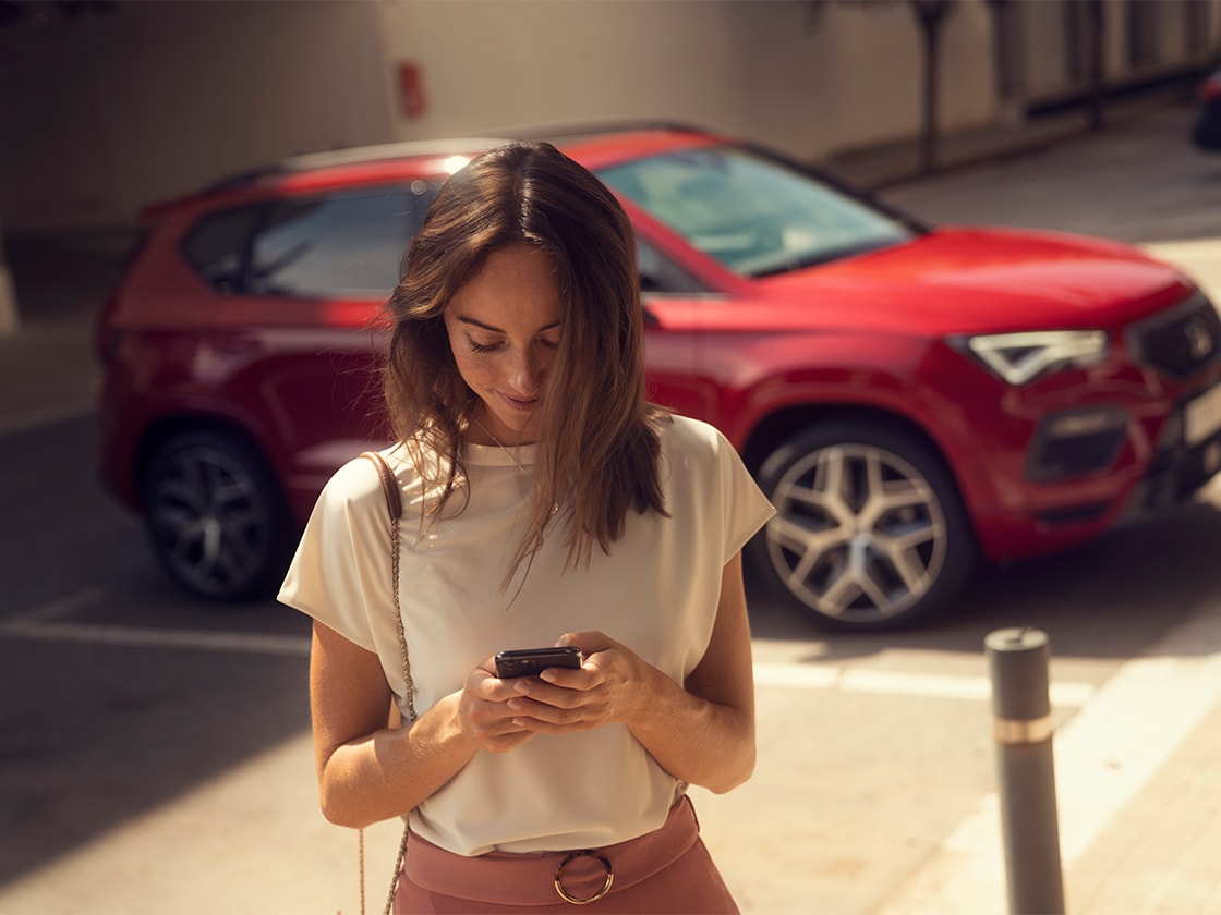 Kobieta ze smartfonem korzystająca z usługi seat connect online obok czerwonego seata ateca.