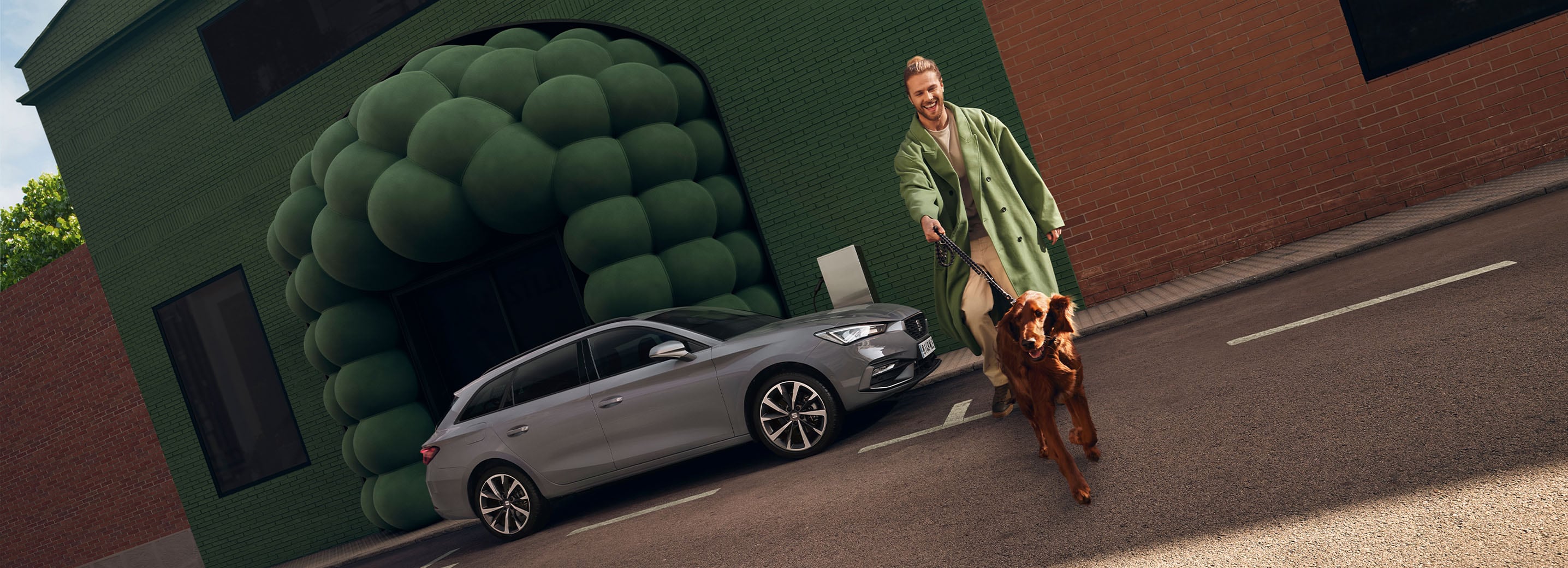 Szary seat leon sportstourer. W pobliżu przechadza się osoba ubrana w te same kolory co tło.