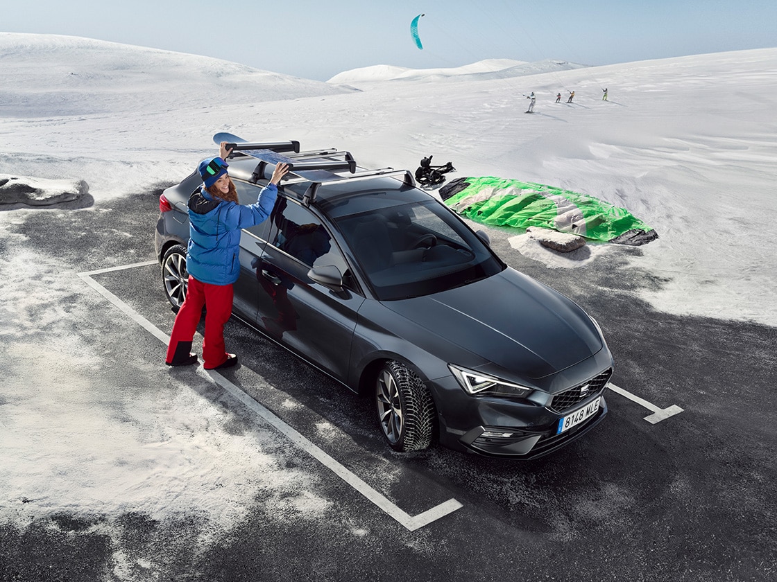 SEAT Leon w górskiej scenerii, z osobą w zimowym stroju korzystającą z bagażnika dachowego.