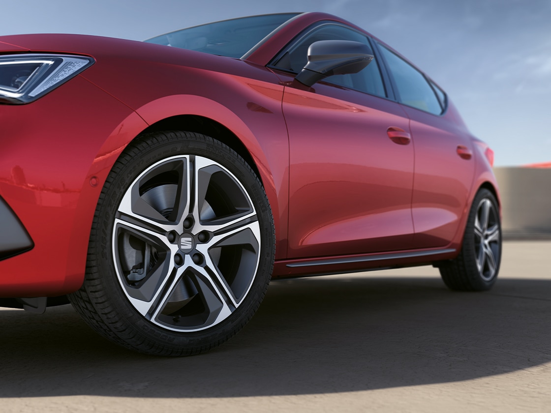 SEAT Leon Sportstourer w kolorze Desire Red, z ujęciem podkreślającym boczną listwę drzwiową i felgę aluminiową, zaparkowany pod bezchmurnym niebem.