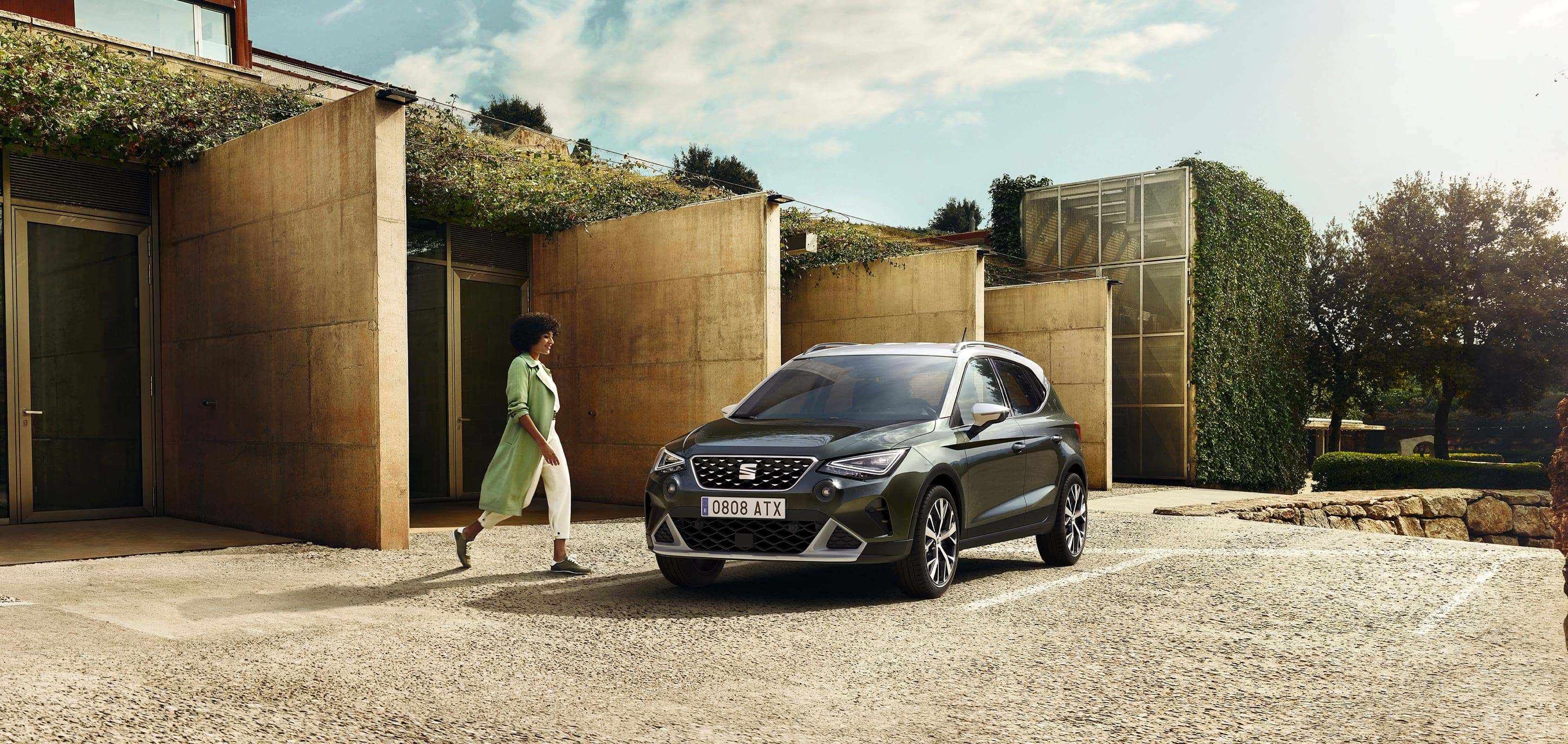 kobieta idzie w kierunku SEAT-a Arona w kolorze dark camouflage z dachem w kolorze candy white