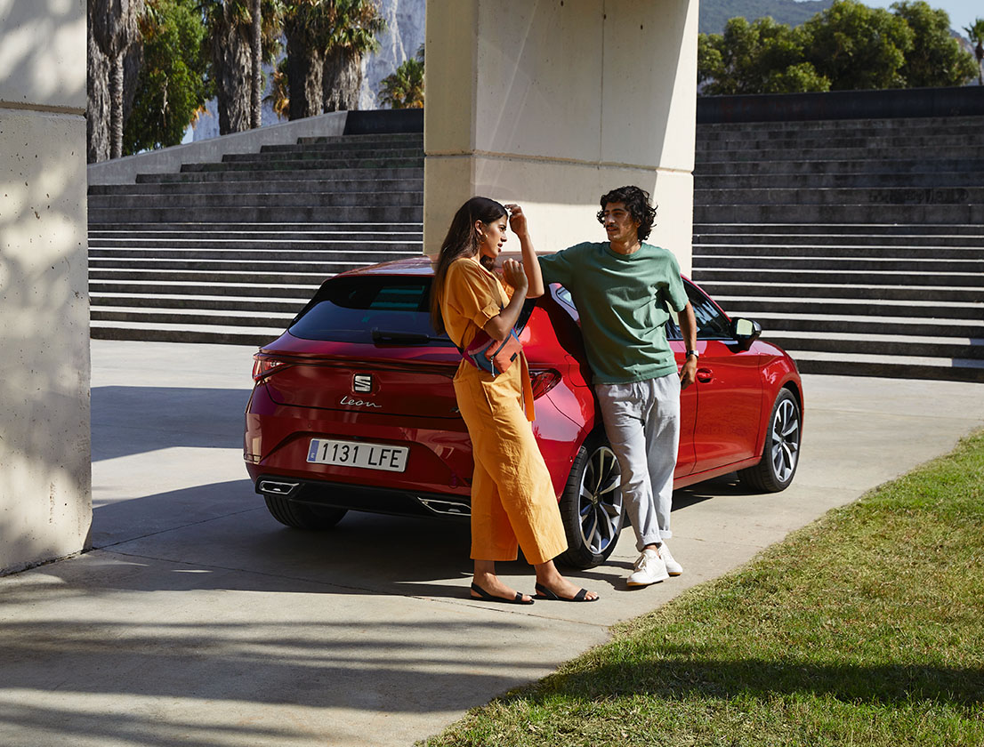 Kobieta i mężczyzna rozmawiają, stojąc obok czerwonego samochodu marki SEAT