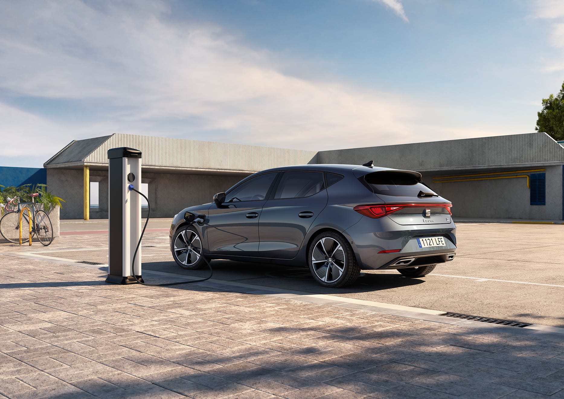 SEAT Leon e-HYBRID w kolorze Magnetic Tech podłączony do ładowarki, widziany z boku. 
