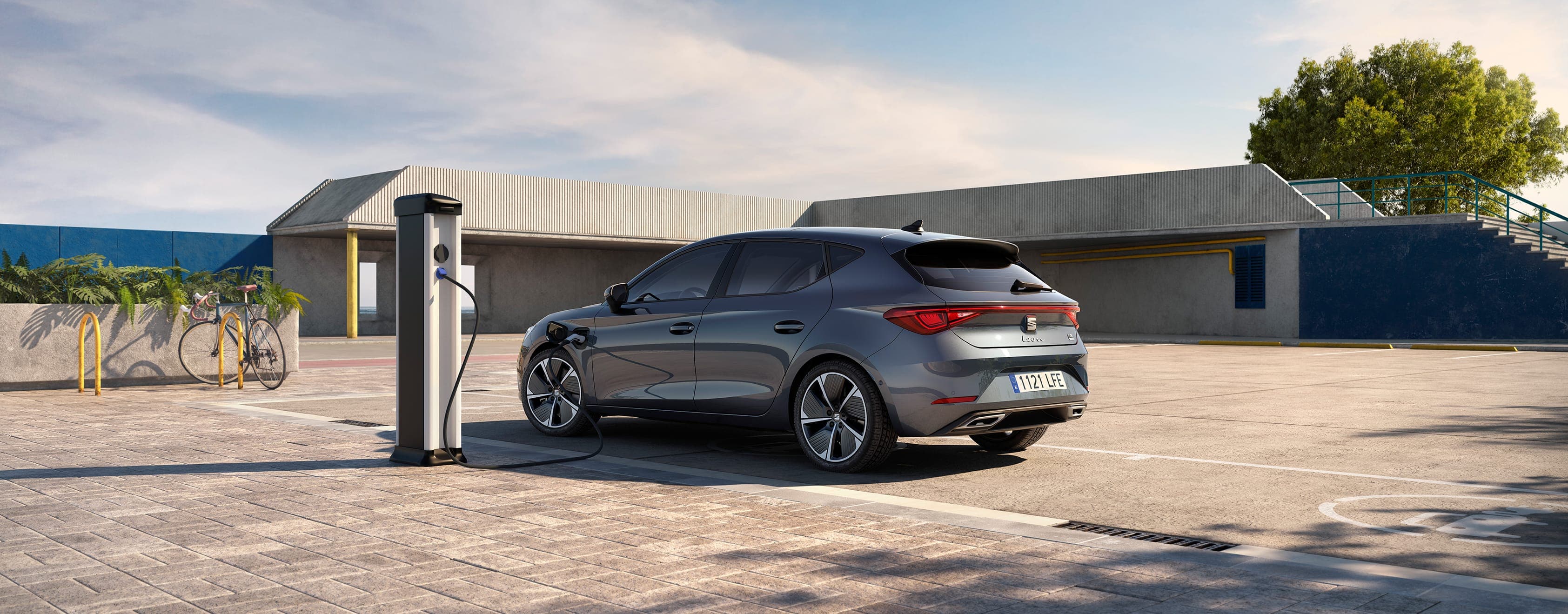 SEAT Leon e-HYBRID w kolorze Magnetic Tech podłączony do ładowarki, widziany z boku. 