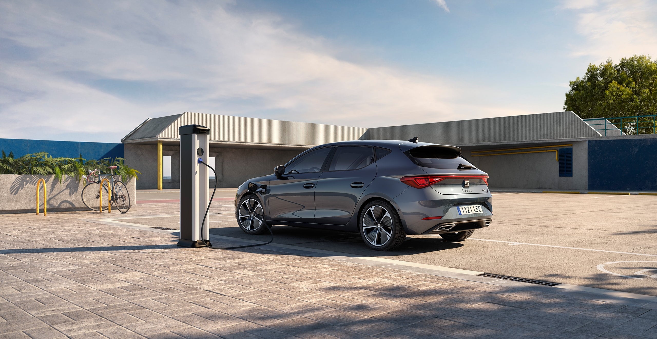 SEAT Leon e-HYBRID w kolorze Magnetic Tech podłączony do ładowarki, widziany z boku. 