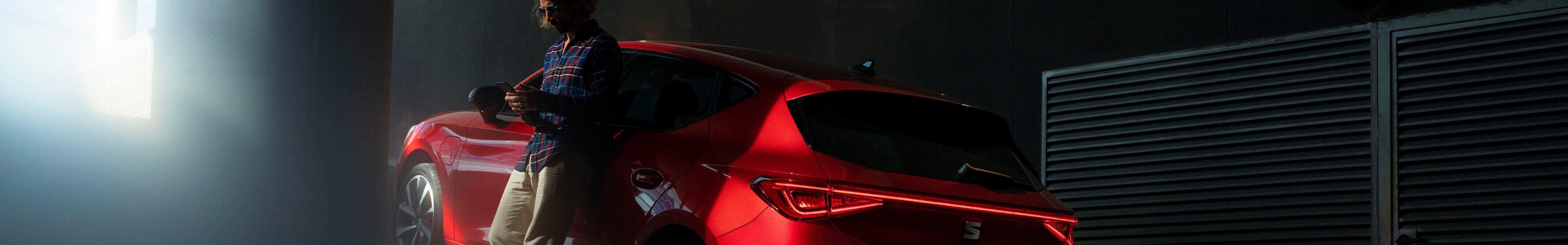 Hybrydowy seat leon sportstourer w kolorze czerwonym, kierowca opierający się o drzwi samochodu 