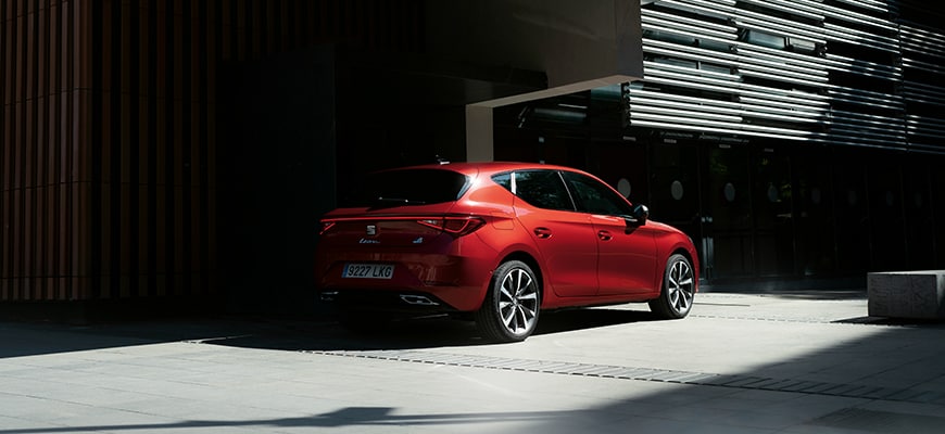 Łagodny hybrydowy pojazd elektryczny seat leon sportstourer w kolorze czerwonym zaparkowany w cieniu przy budynku