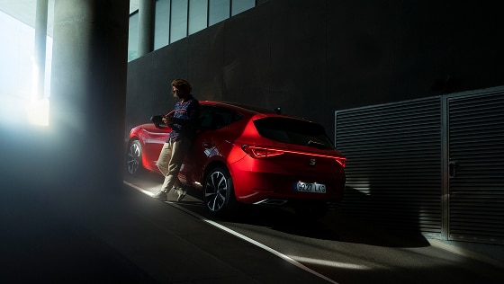 Widok z tyłu czerwonego Leona 5D plug in hybrid, na krytym parkingu, z mężczyzną opierającym się o samochód