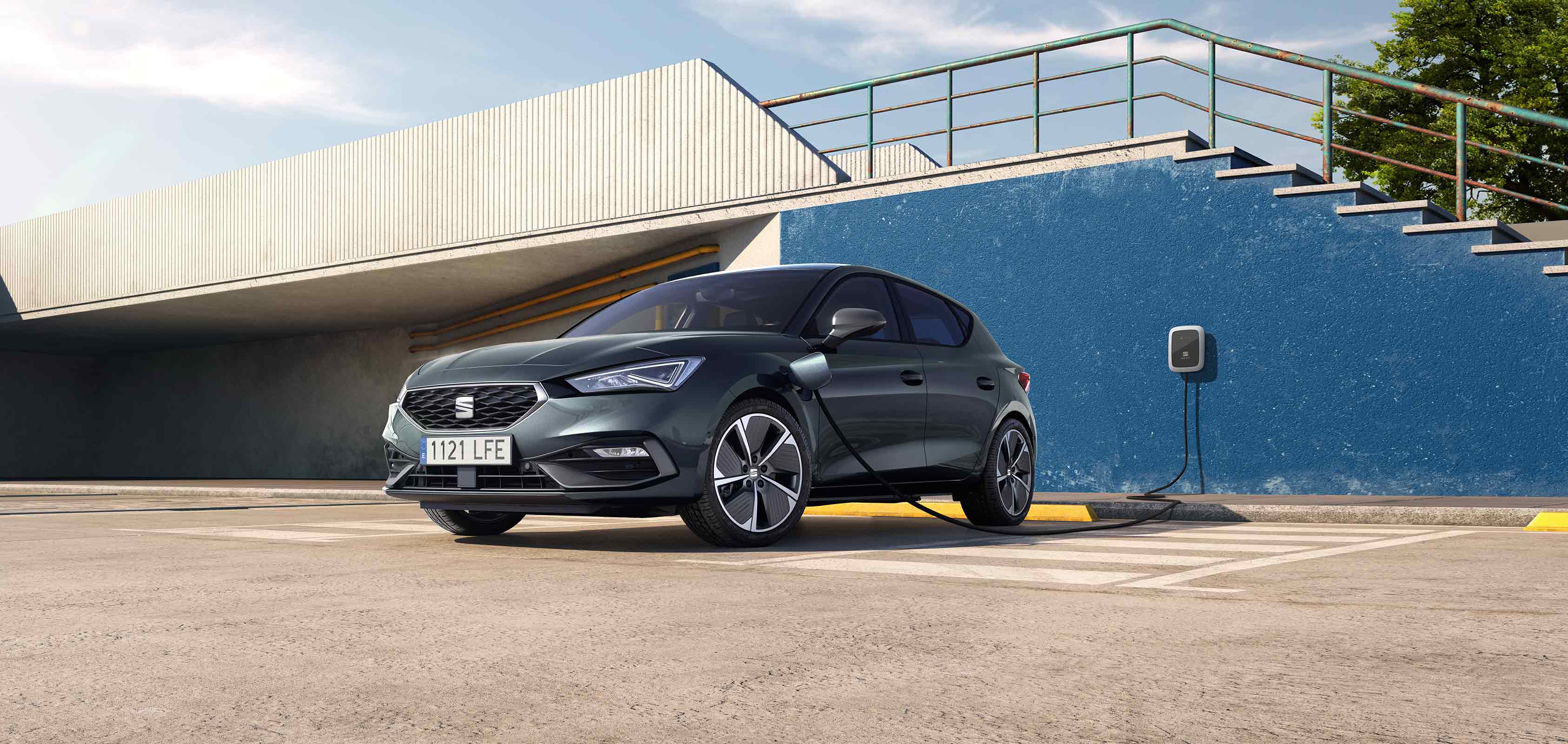 SEAT Leon e-HYBRID w kolorze Midnight Black podłączony do ładowarki, widziany z boku. 