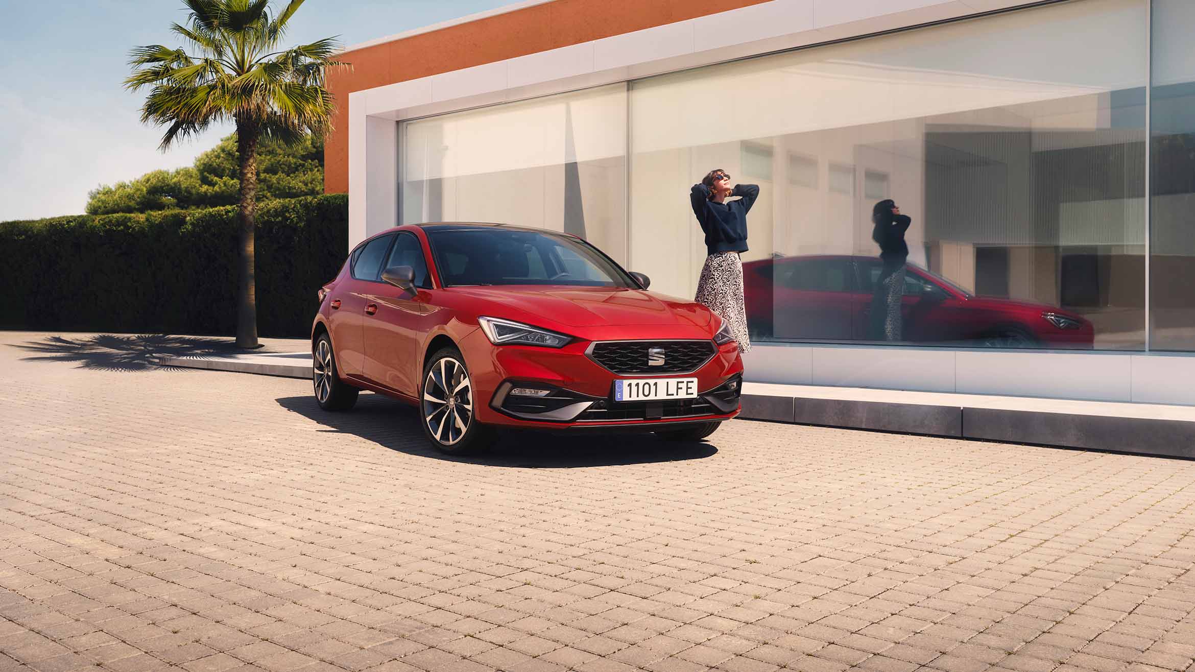 SEAT Leon 5D w kolorze Desire Red na tle nowoczesnego budynku